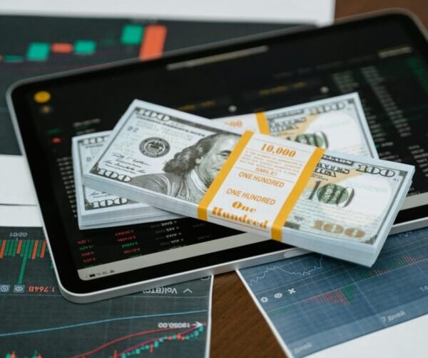 Stack of $100 bills placed on a tablet with financial graphs, symbolizing digital finance.
